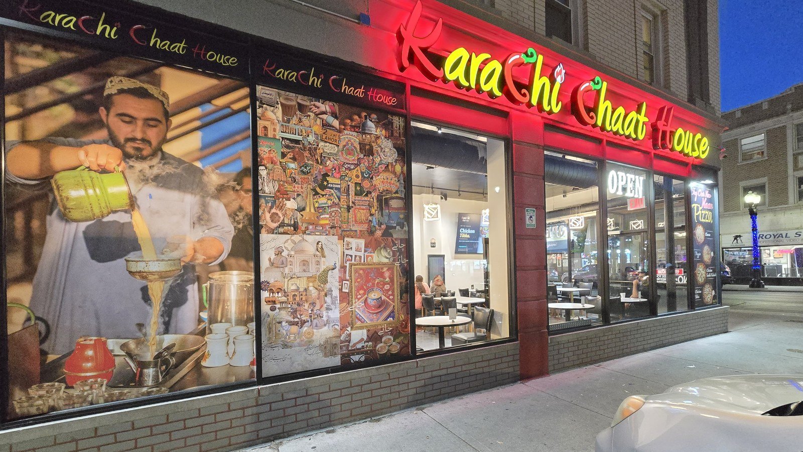 Karachi Chaat House storefront at night on Devon Avenue, Chicago — neon sign glowing red and yellow with diners visible through the window